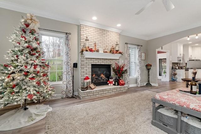 living room with hardwood / wood-style flooring, ceiling fan, ornamental molding, and a brick fireplace