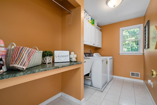 clothes washing area featuring washing machine and dryer, light tile patterned flooring, and cabinets