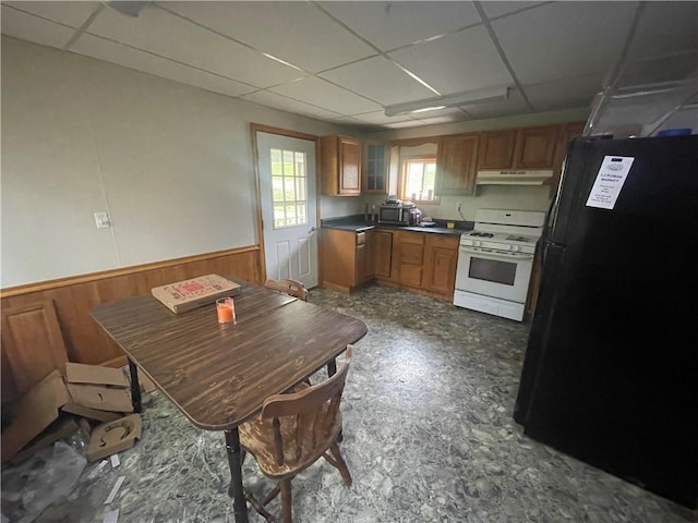 kitchen with a paneled ceiling, black fridge, white gas stove, and wood walls