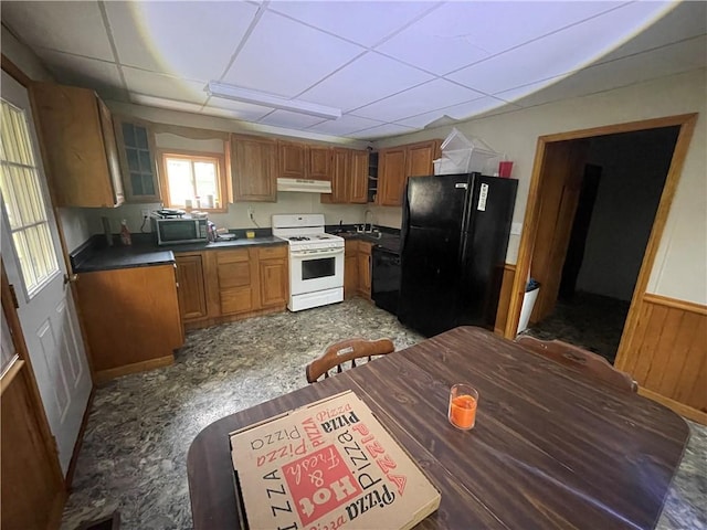 kitchen with black appliances, a paneled ceiling, wood walls, and sink
