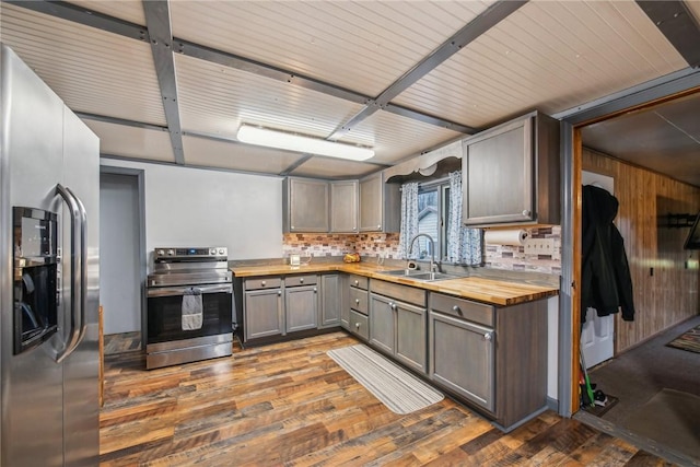 kitchen with decorative backsplash, appliances with stainless steel finishes, dark hardwood / wood-style flooring, sink, and butcher block countertops