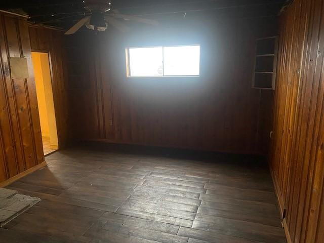 unfurnished room featuring wooden walls, ceiling fan, and dark wood-type flooring