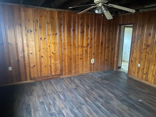 spare room featuring ceiling fan, dark wood-type flooring, and wooden walls