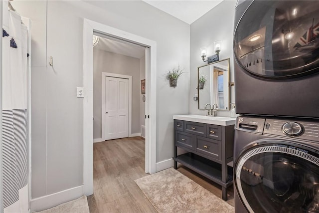 laundry area featuring light hardwood / wood-style flooring, stacked washing maching and dryer, and sink