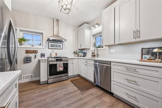 kitchen featuring white cabinetry, light hardwood / wood-style flooring, wall chimney exhaust hood, and appliances with stainless steel finishes