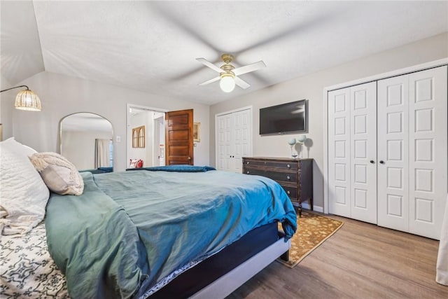 bedroom featuring vaulted ceiling, ceiling fan, hardwood / wood-style floors, and two closets