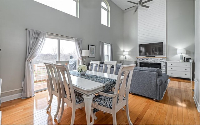 dining area featuring a fireplace, a towering ceiling, light hardwood / wood-style flooring, and ceiling fan