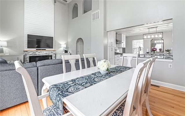 dining space featuring a fireplace, light hardwood / wood-style flooring, and a high ceiling