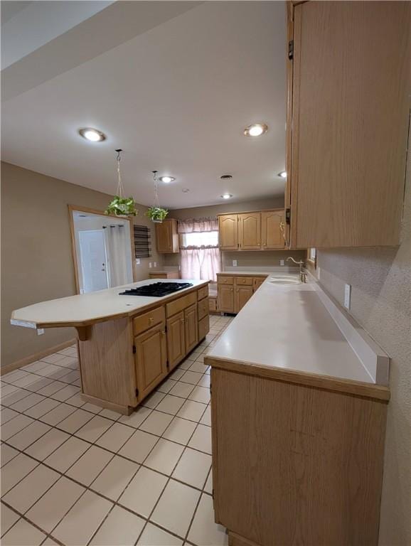 kitchen featuring a center island, sink, gas stovetop, light brown cabinetry, and a kitchen bar