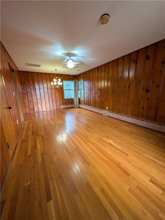 interior space with wooden walls, a baseboard radiator, ceiling fan with notable chandelier, and light wood-type flooring