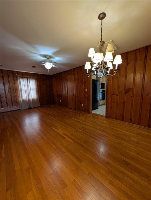 unfurnished dining area featuring hardwood / wood-style floors, ceiling fan with notable chandelier, and wooden walls