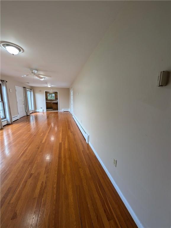 unfurnished living room with ceiling fan, light hardwood / wood-style floors, and a baseboard heating unit