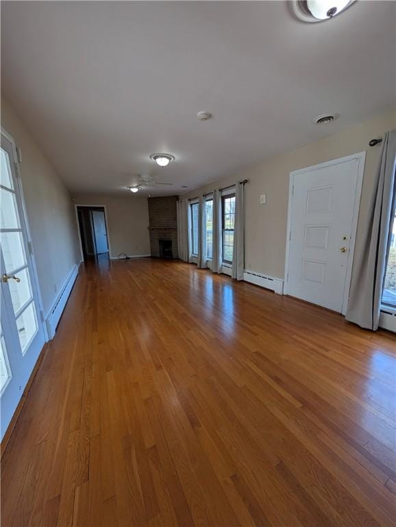 unfurnished living room featuring wood-type flooring, a fireplace, and a baseboard heating unit