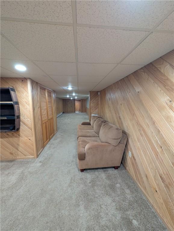 carpeted living room with a drop ceiling and wood walls