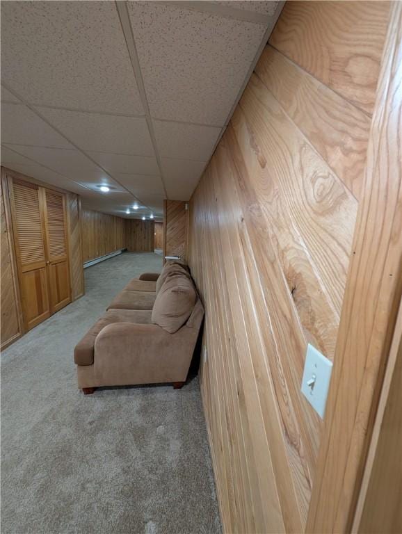 carpeted living room featuring baseboard heating, a drop ceiling, and wooden walls