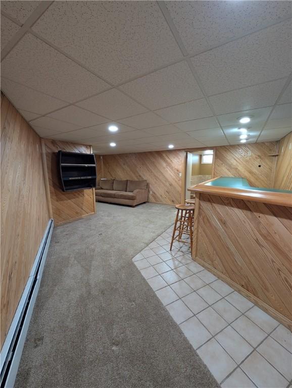 bar featuring tile patterned flooring, a baseboard radiator, a drop ceiling, and wooden walls