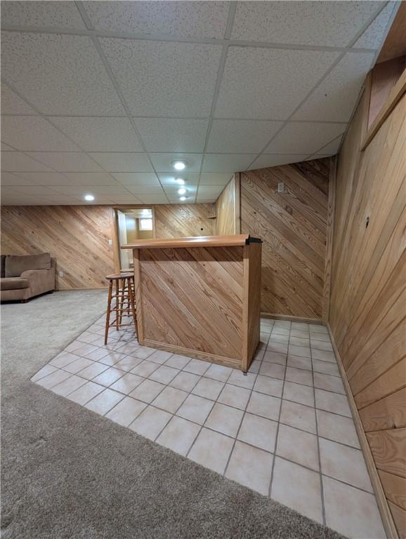 bar featuring a paneled ceiling, light colored carpet, and wooden walls