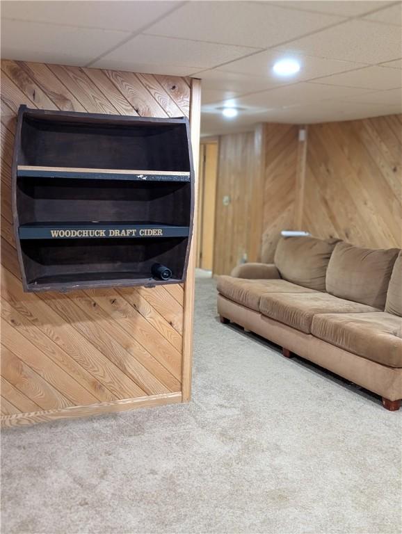 carpeted living room with a paneled ceiling and wood walls