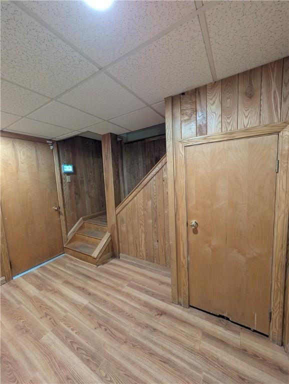 basement with a paneled ceiling, light hardwood / wood-style flooring, and wood walls