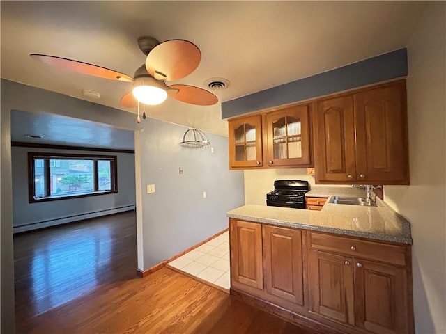 kitchen with ceiling fan, sink, a baseboard radiator, black gas range oven, and light hardwood / wood-style floors