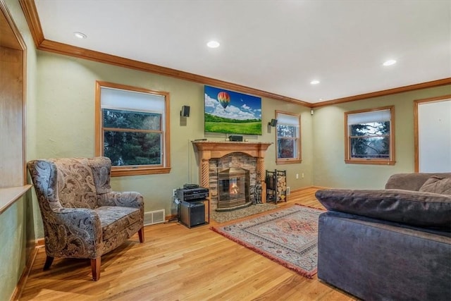 living room with a stone fireplace, crown molding, and light hardwood / wood-style flooring