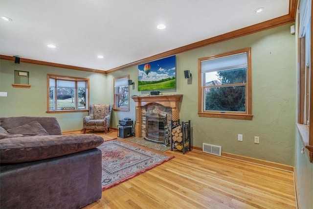 living room featuring light hardwood / wood-style floors, a stone fireplace, and ornamental molding