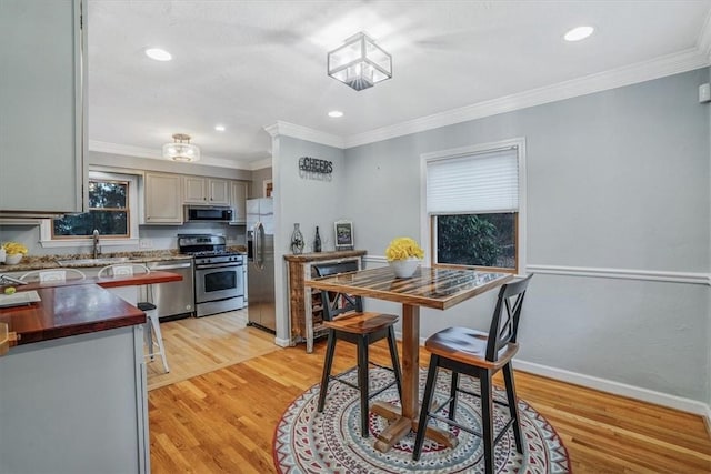 kitchen with light wood-type flooring, stainless steel appliances, ornamental molding, and sink