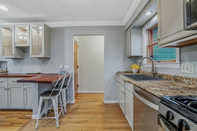 kitchen featuring sink, stainless steel appliances, wood counters, light wood-type flooring, and ornamental molding