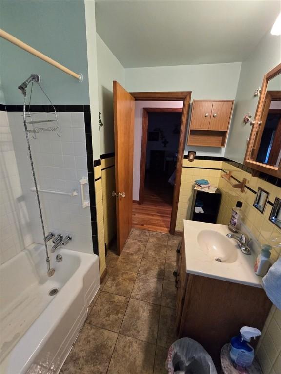 bathroom with tile patterned floors, vanity, washtub / shower combination, and tile walls