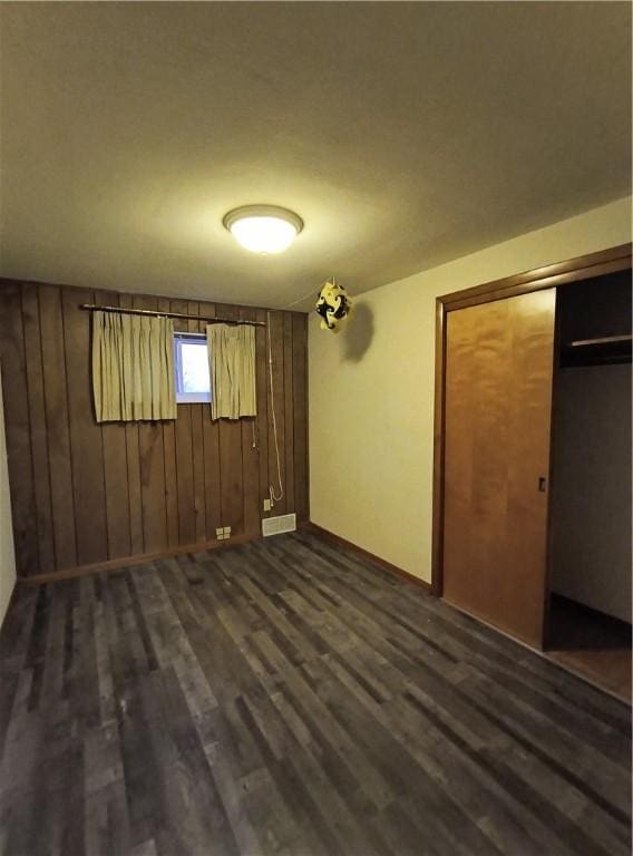 unfurnished bedroom with wood walls, dark wood-type flooring, and a closet