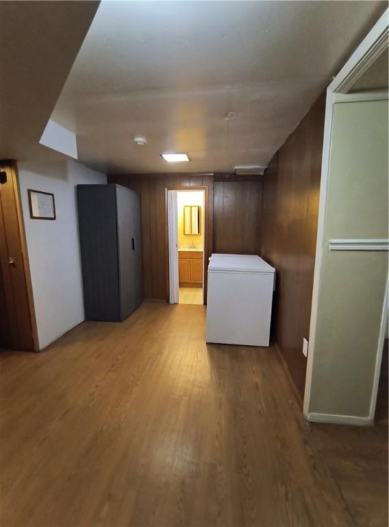 basement featuring light wood-type flooring, fridge, and wood walls