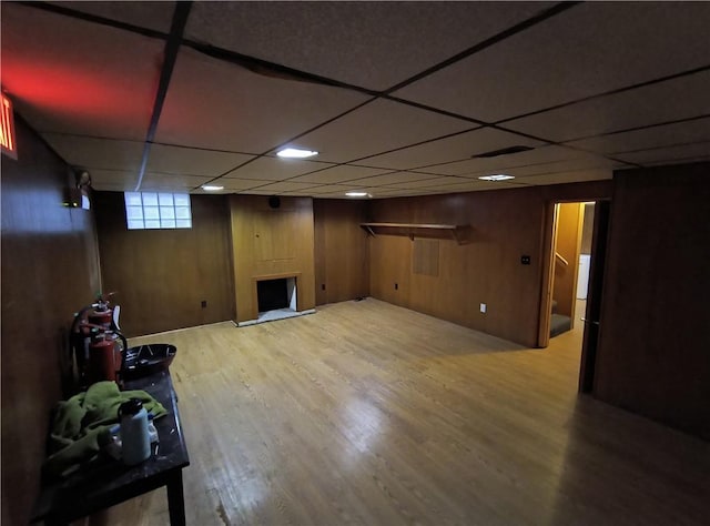 basement with hardwood / wood-style floors, a paneled ceiling, and wooden walls