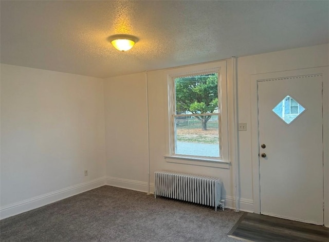 foyer entrance featuring dark carpet, radiator heating unit, and a textured ceiling