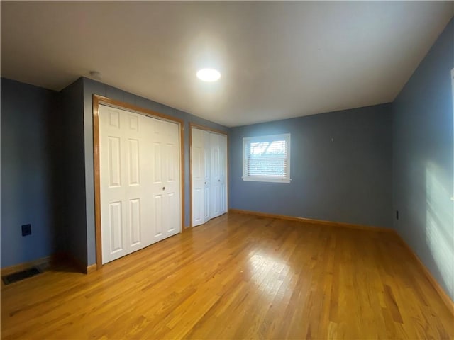 unfurnished bedroom featuring two closets and light hardwood / wood-style flooring