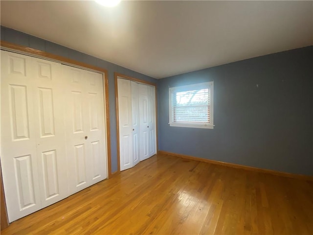 unfurnished bedroom with light hardwood / wood-style flooring and two closets