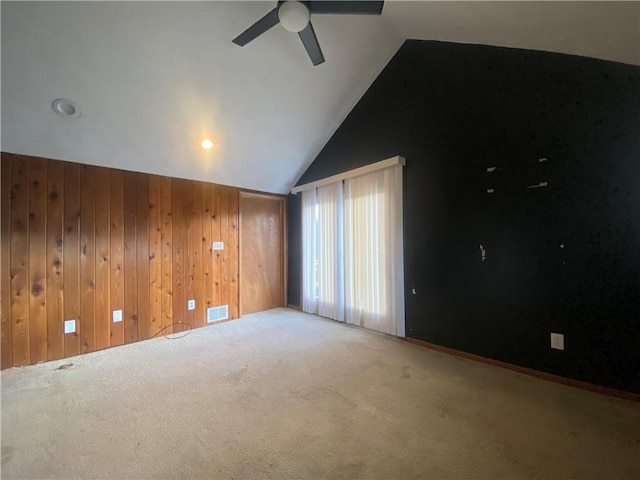 spare room featuring carpet flooring, ceiling fan, wood walls, and lofted ceiling