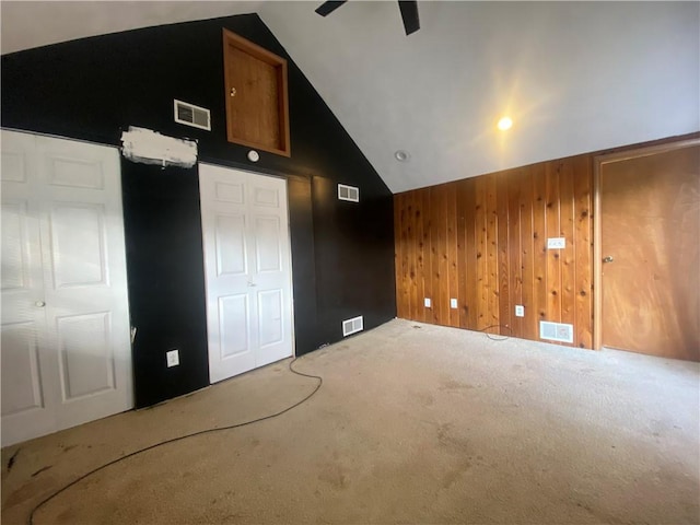 interior space with carpet floors, high vaulted ceiling, ceiling fan, and wood walls