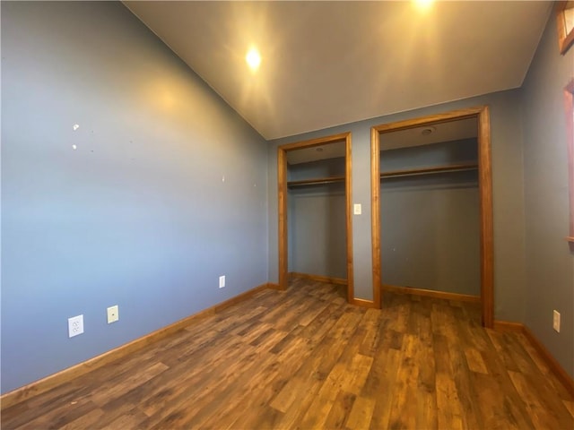 unfurnished bedroom with multiple closets, dark wood-type flooring, and vaulted ceiling