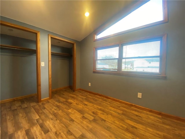 unfurnished bedroom with wood-type flooring, two closets, and lofted ceiling