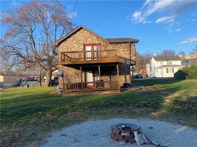 back of house featuring a fire pit, a wooden deck, and a lawn