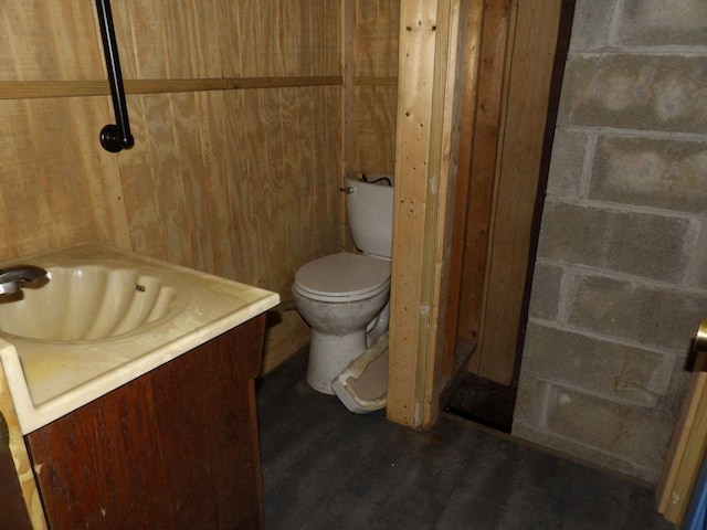 bathroom with hardwood / wood-style flooring, wooden walls, vanity, and toilet