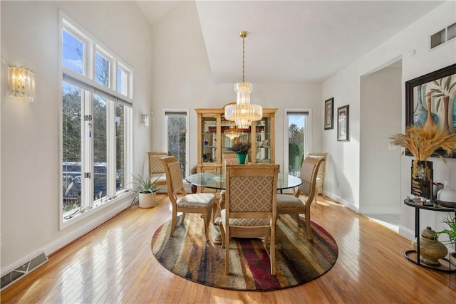 dining area with a notable chandelier, light wood-type flooring, and lofted ceiling