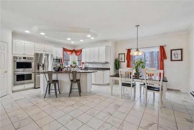 kitchen featuring white cabinets, appliances with stainless steel finishes, a breakfast bar, and decorative light fixtures