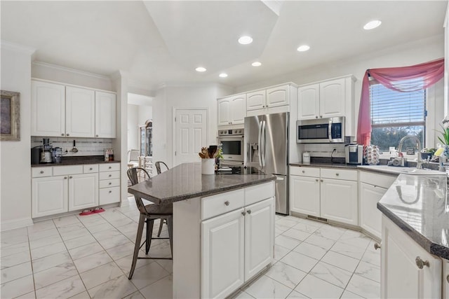 kitchen with white cabinetry, a center island, stainless steel appliances, backsplash, and crown molding