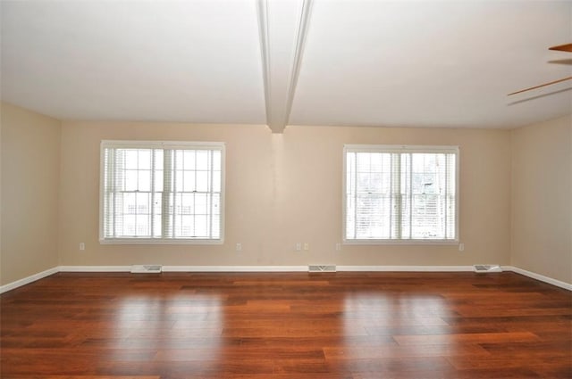 spare room featuring ceiling fan, dark wood-type flooring, and beam ceiling