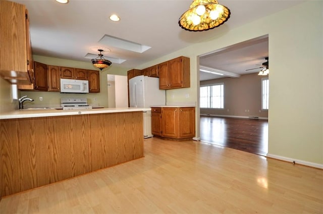 kitchen with light wood-type flooring, kitchen peninsula, white appliances, and pendant lighting