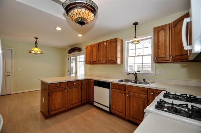 kitchen featuring light hardwood / wood-style floors, kitchen peninsula, decorative light fixtures, white appliances, and sink