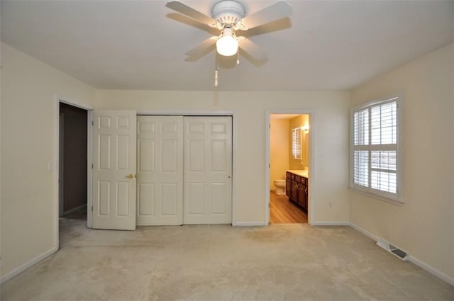 unfurnished bedroom featuring a closet, ceiling fan, light colored carpet, and ensuite bath