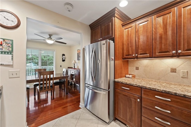 kitchen with tasteful backsplash, light stone counters, stainless steel fridge, light hardwood / wood-style floors, and ornamental molding