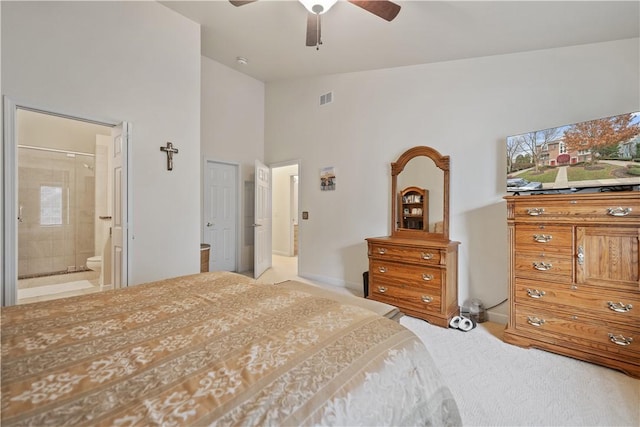 bedroom featuring ceiling fan, ensuite bathroom, a towering ceiling, and light carpet